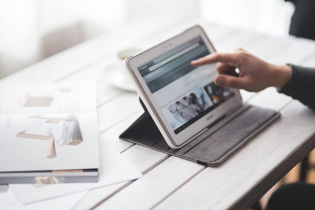 Person using white tablet that is sitting on a tabletop.