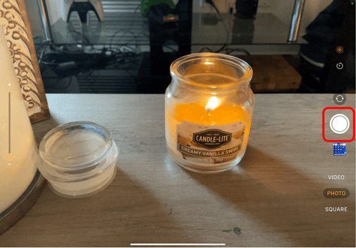 Camera on iPad pointing at a candle with the white button circled in red to show how to take a photo using the Camera app