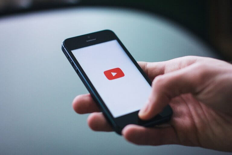 Hand holding smartphone with YouTube logo on the screen.