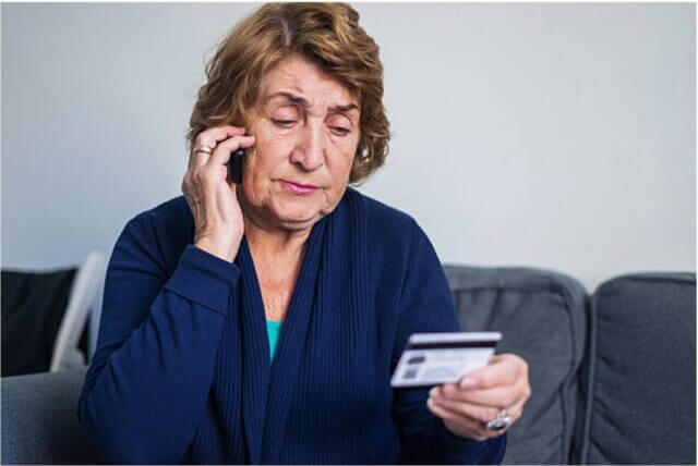 Older woman looking at bank card with worried expression on face.